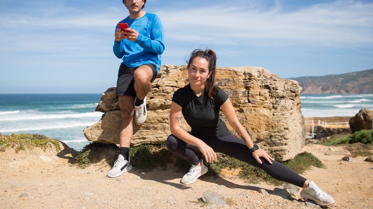 A couple stretching and using a phone on a scenic beach in Portugal.