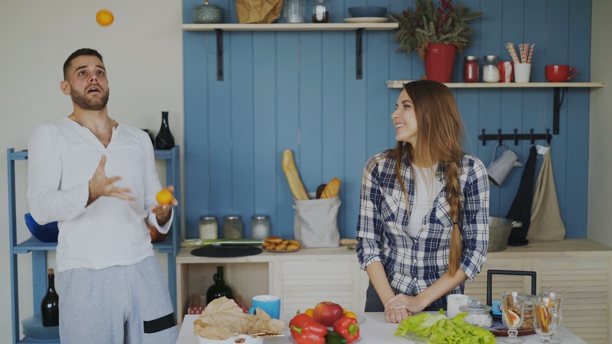 Attractive loving couple having fun in the kitchen. Handsome man juggle with fruits to impress his girlfriend at home
